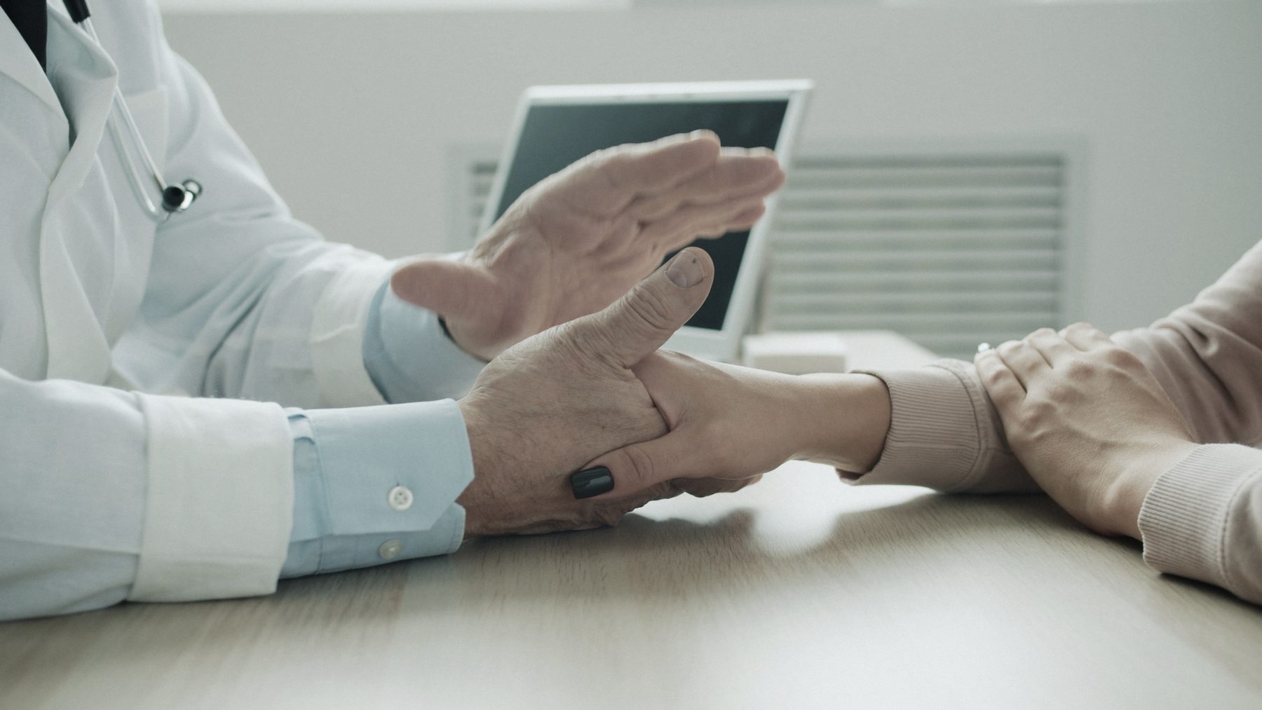 A doctor’s hand resting on a patient’s arm across a desk