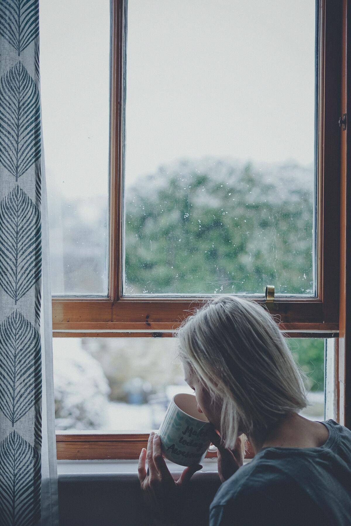 A woman holding a mug, sitting by a window with trees outside