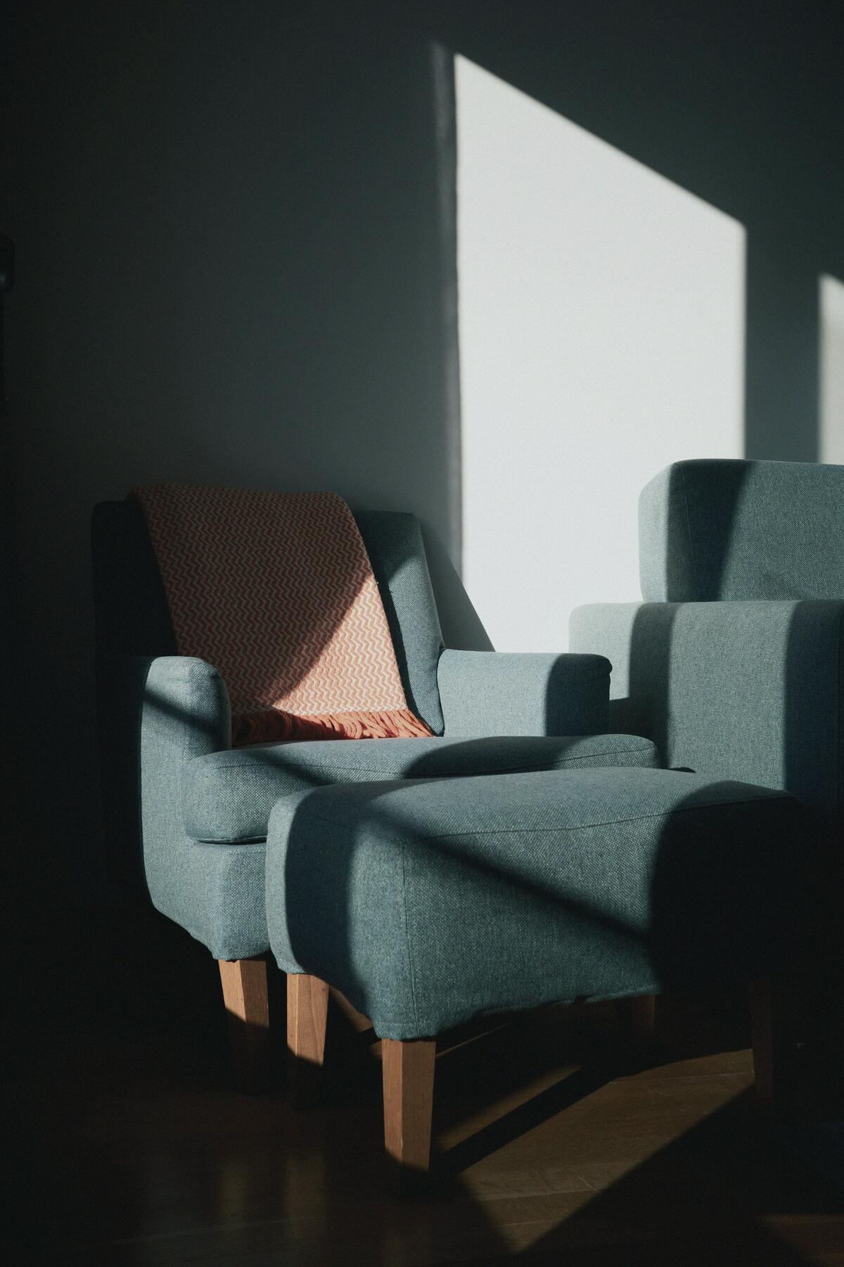 A teal armchair and footstool in a stripe of afternoon sun