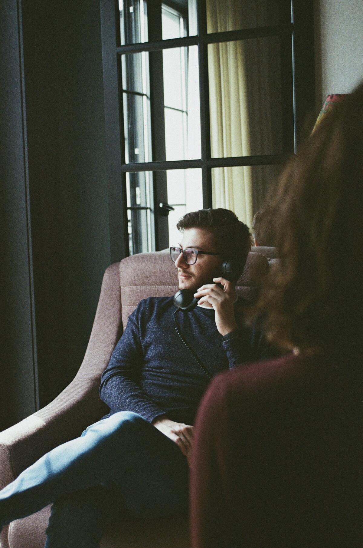 A man in a blue jumper sitting in a brown armchair, talking