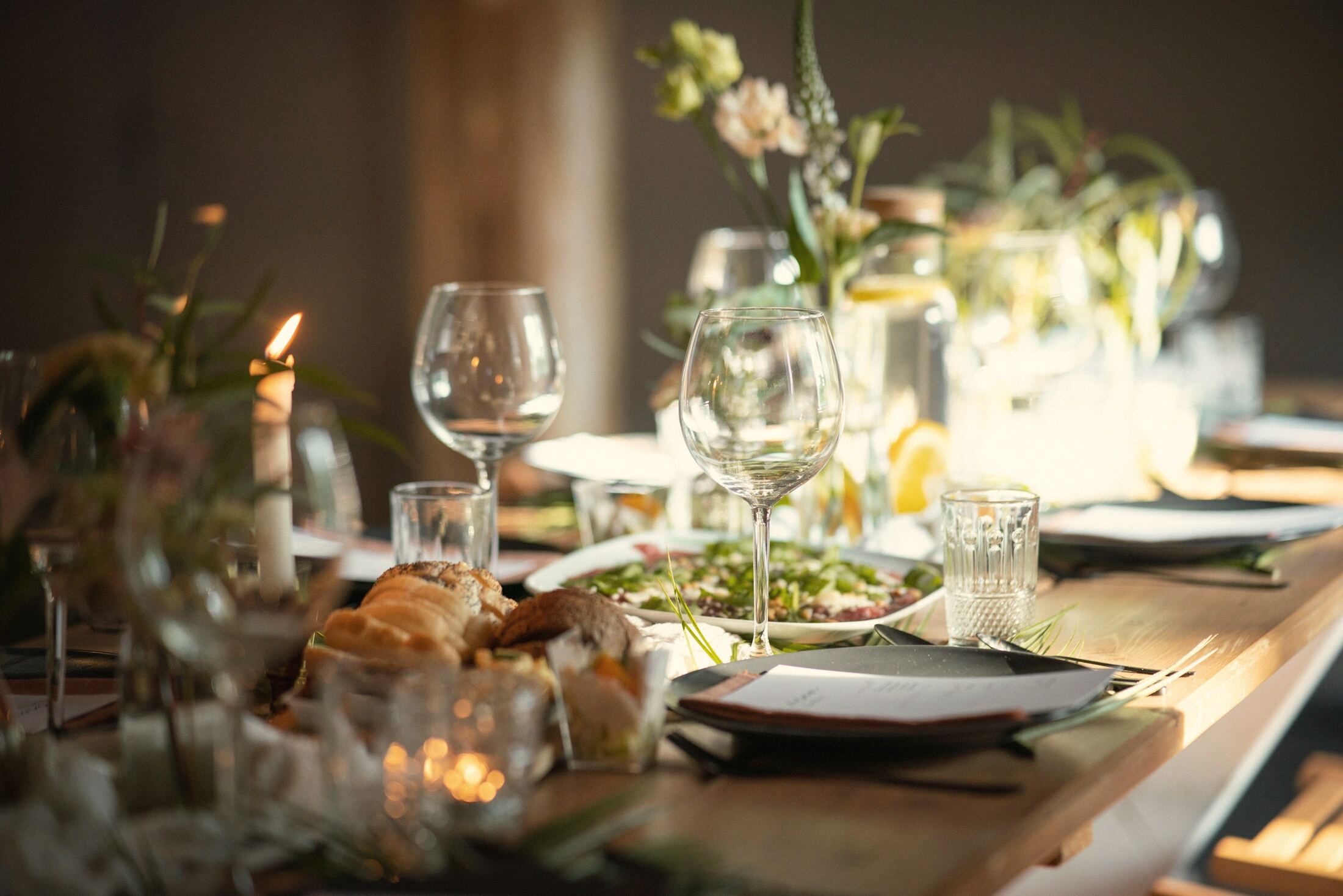 A long table set with candles, glasses and bread in warm evening light