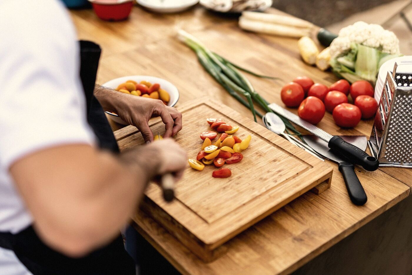 A cook cutting tomatoes and vegetables on a board
