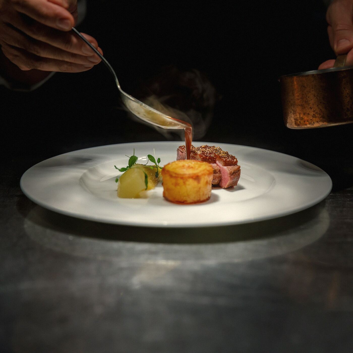 A chef spooning sauce onto a plated dish
