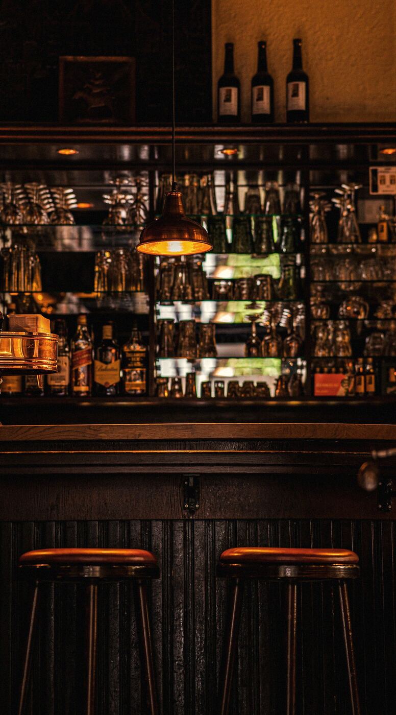 A dim bar with a lit bottle rack and stools