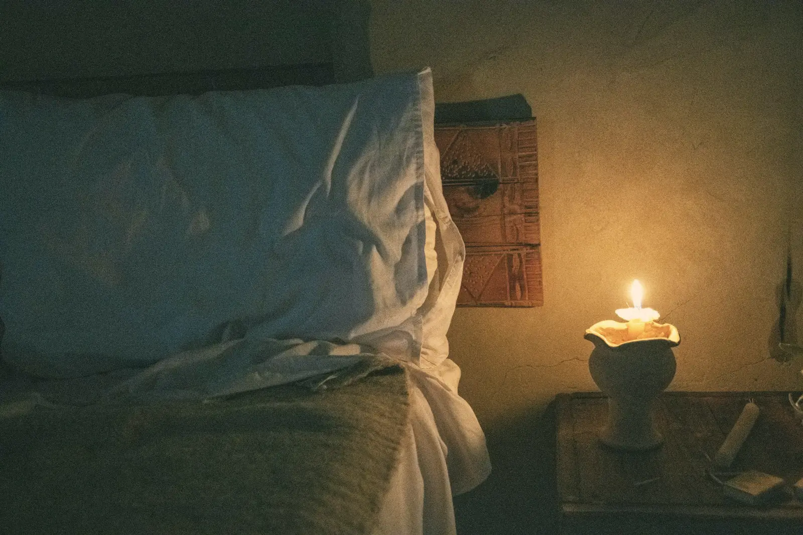 A candle on a nightstand beside a bed