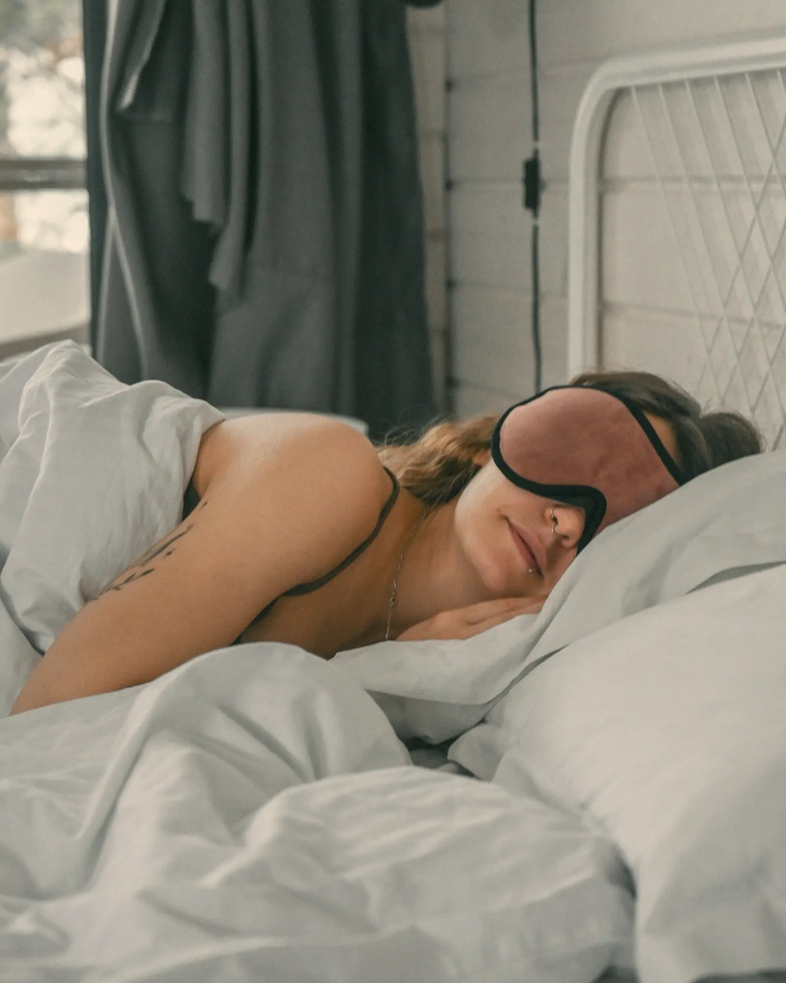 A woman asleep with an eye mask in white sheets