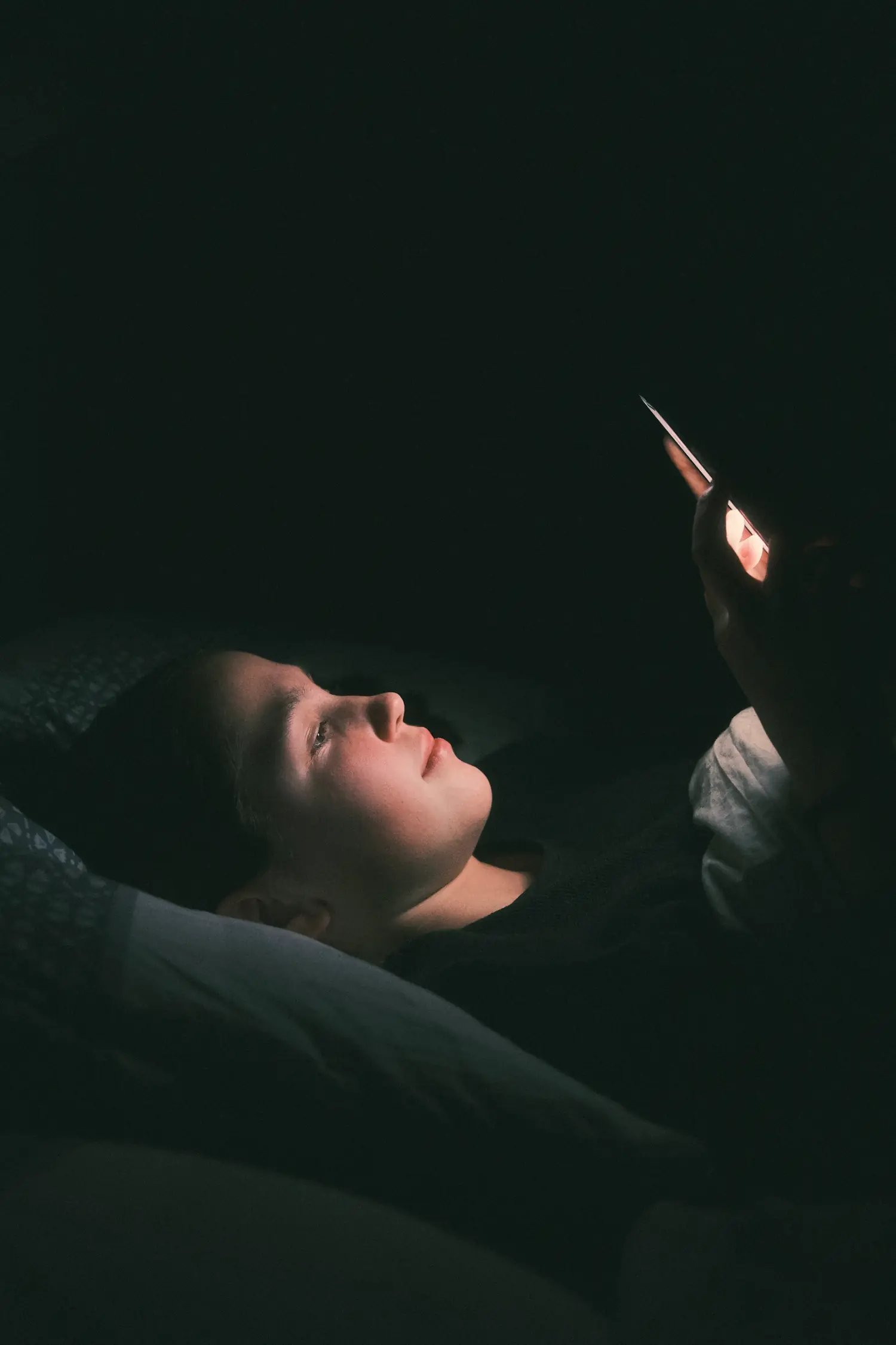 A woman lying in bed in the dark, her face lit by her phone