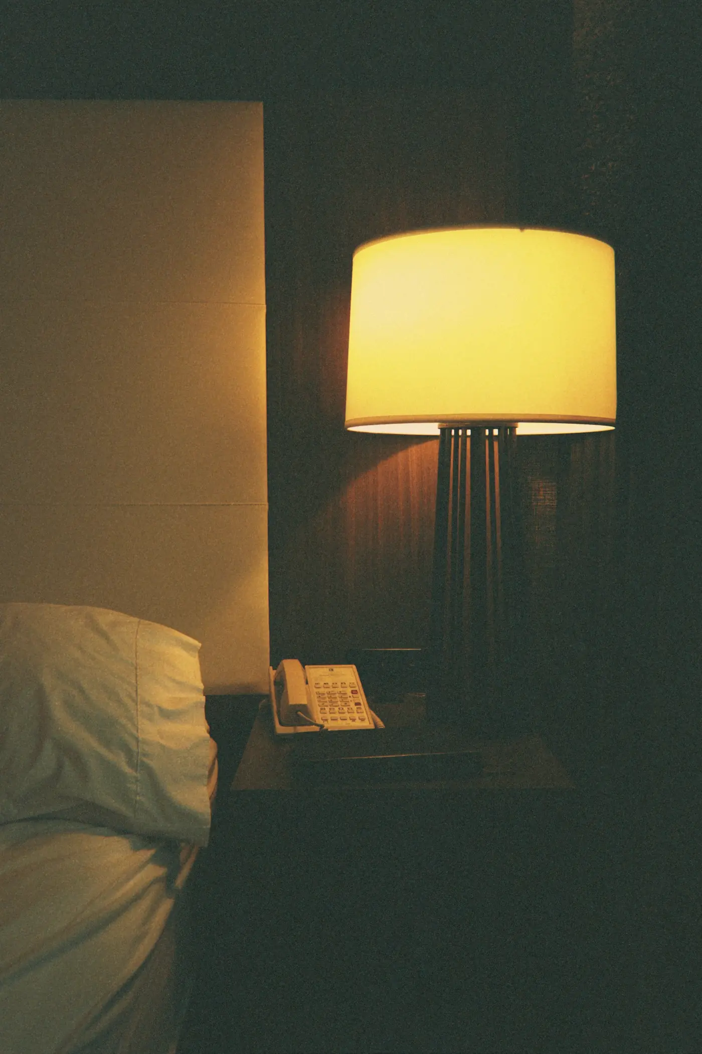 A warm lamp on in a dark bedroom