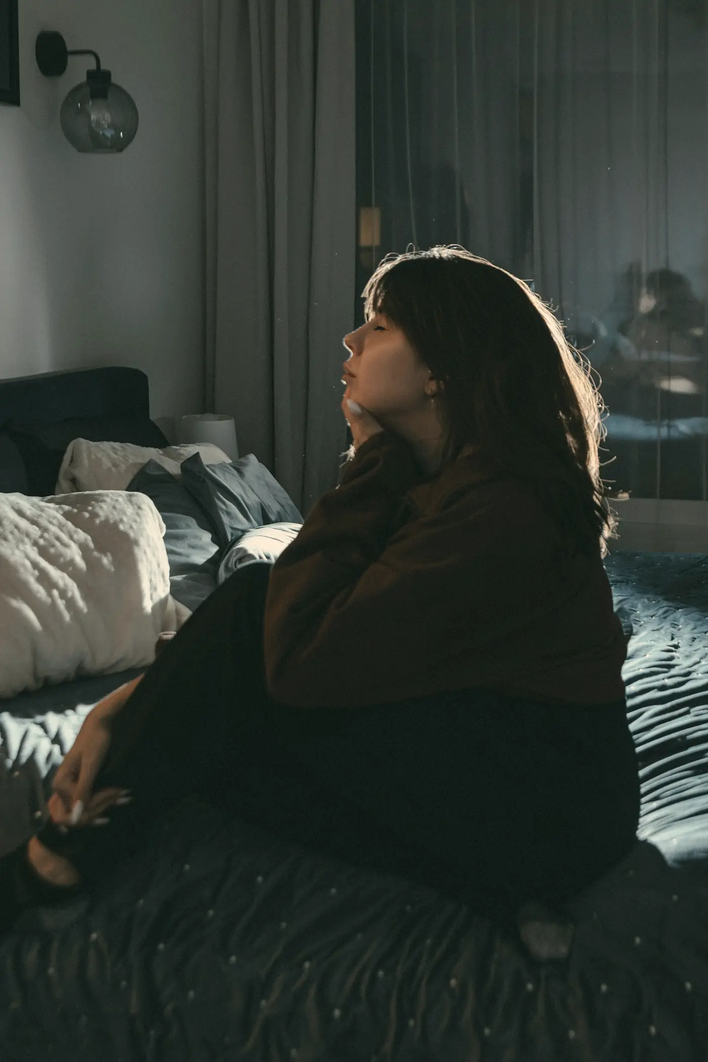 A woman sitting on her bed in a dim room