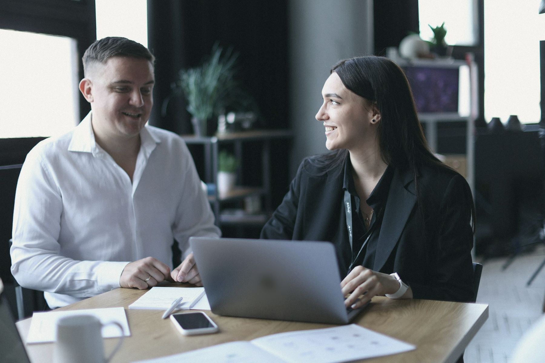 An adviser and a client laughing over a laptop at a meeting table