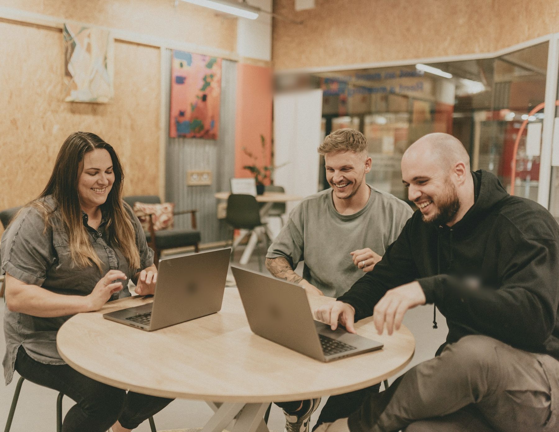 Three colleagues laughing around a small table with laptops