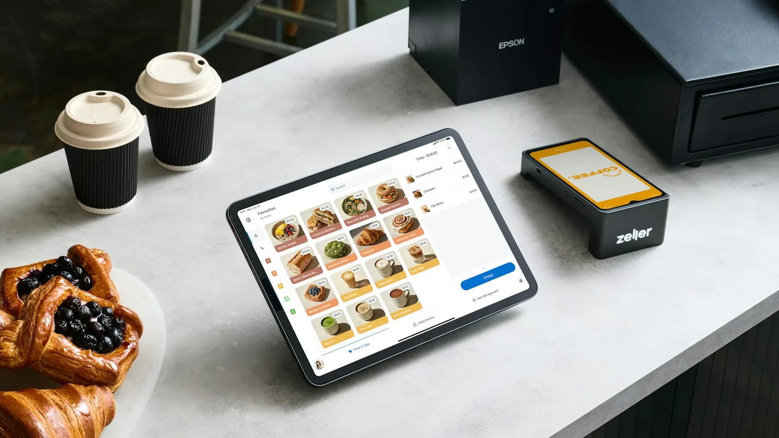 A tablet point of sale system with pastries and coffee on a counter